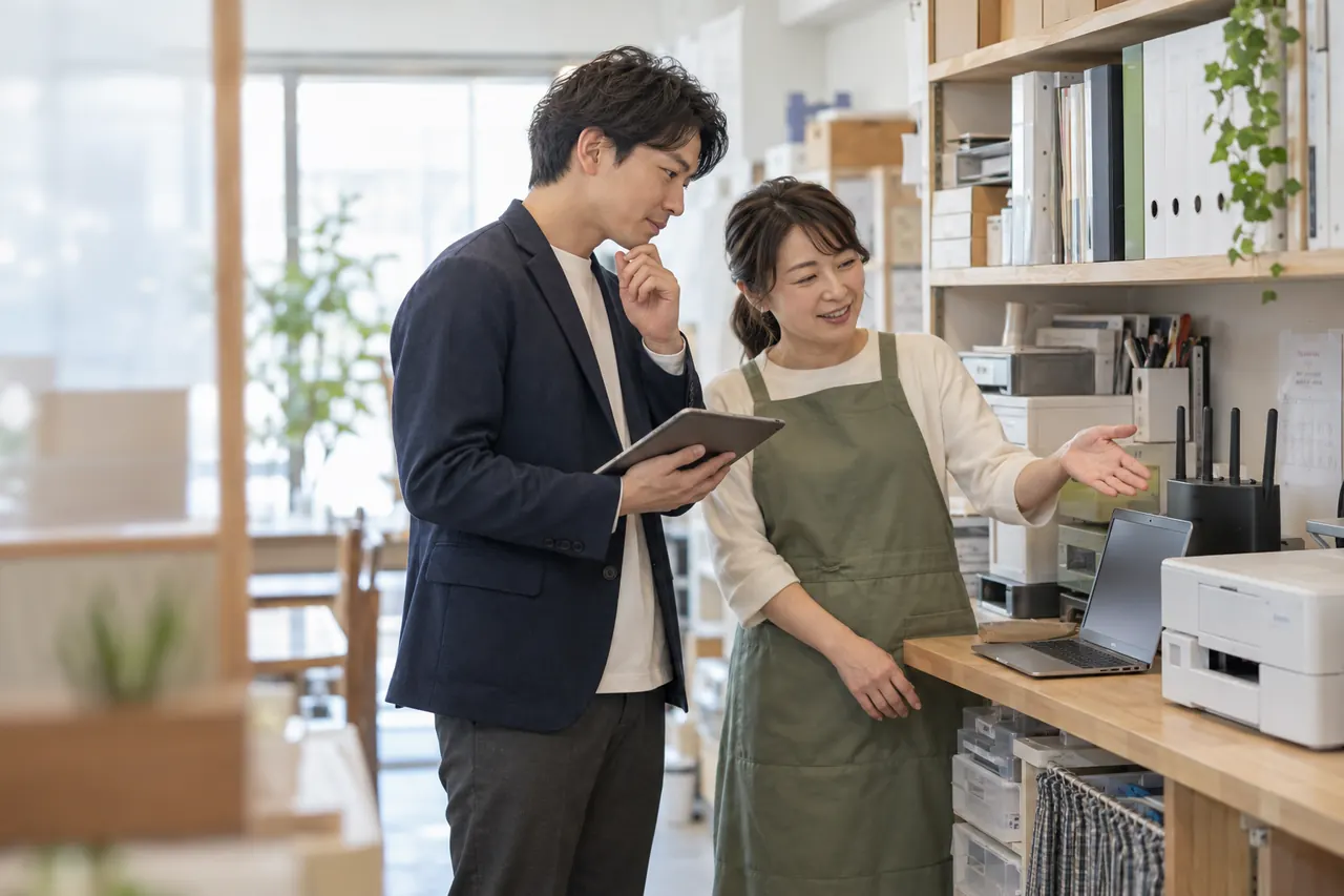 店舗のPCや周辺機器を見ながら困りごとを相談する店主とIT担当者